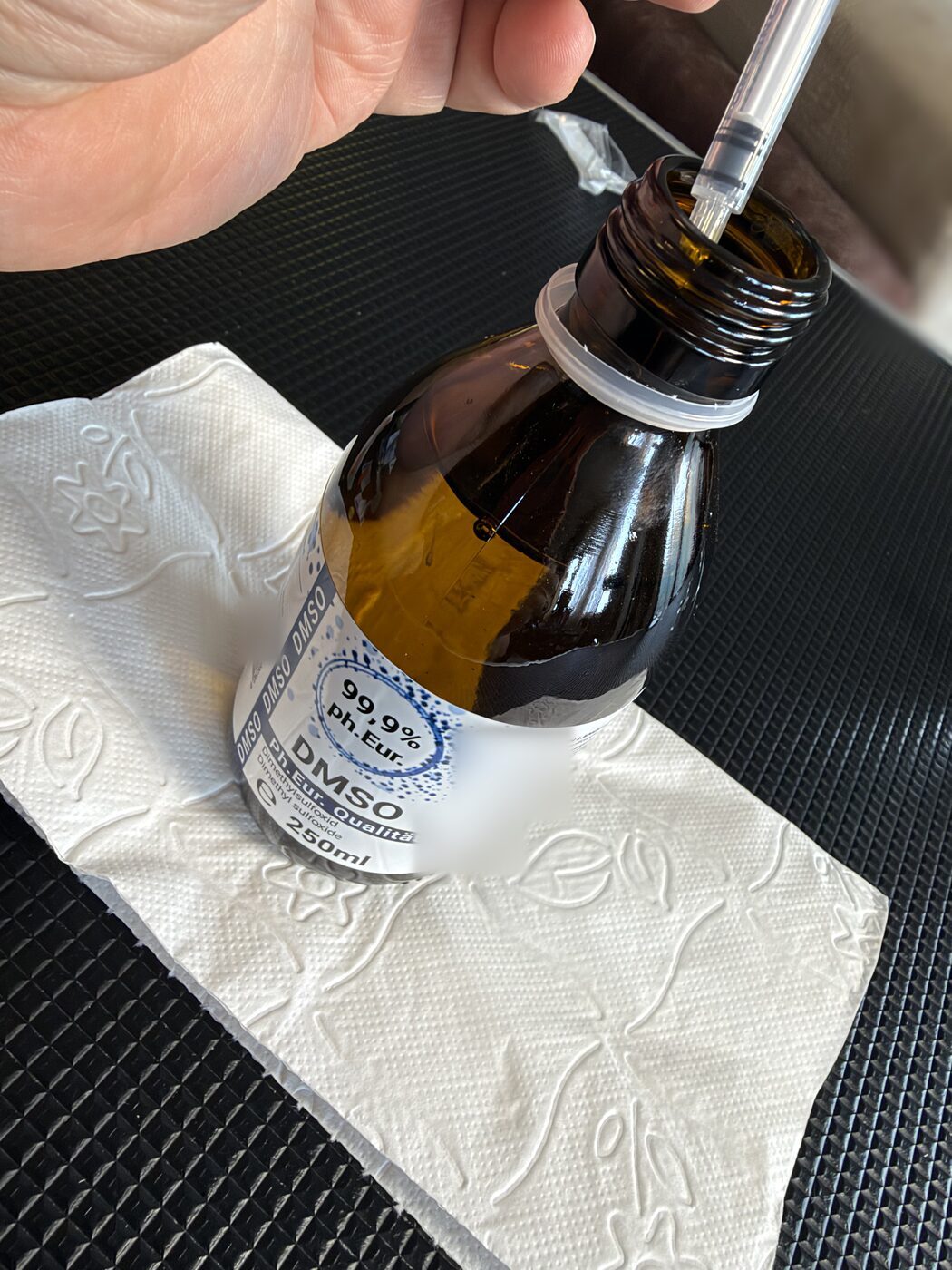 Strzykawka insulinowa trzymana w szyjce brązowej szklanej butelki z DMSO stojącej na ręczniku papierowym